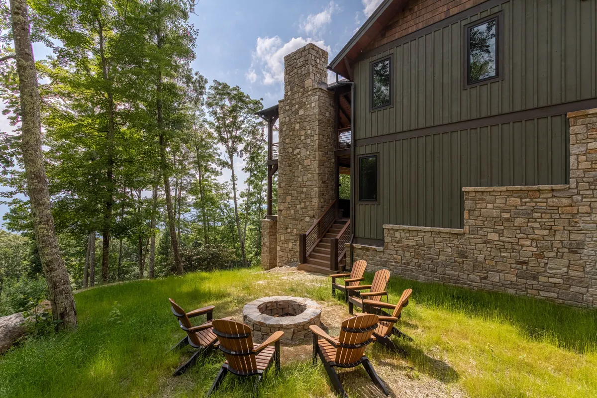A cozy fire pit area with wooden chairs, a stone chimney, and surrounding trees, creating a welcoming outdoor gathering spot that captures the spirit of mountain relaxation after a day of activity.