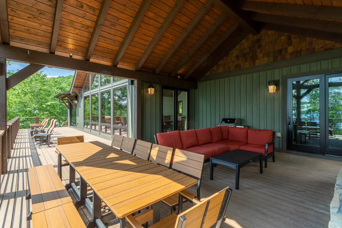 An exterior shot of a large outdoor seating area with a dining table overlooking lush greenery. The space is designed for outdoor dining, relaxing with friends, and entertaining guests, with natural light and open-air ambiance perfect for food and wine enjoyment.