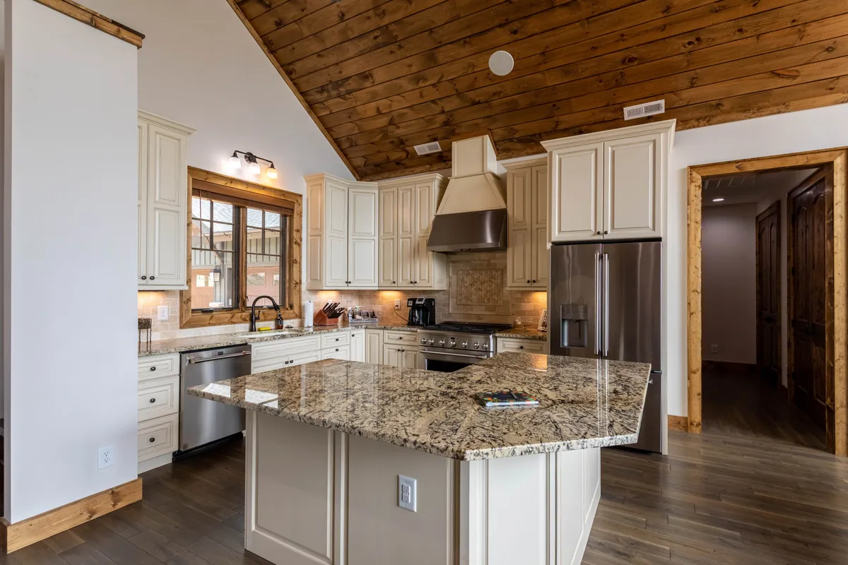 This interior image features a gourmet kitchen with granite countertops, wooden ceiling, stainless steel appliances, and custom cabinetry. The layout highlights ample workspace and modern amenities ideal for cooking, entertaining, and gathering with family or friends for holiday or celebratory meals.