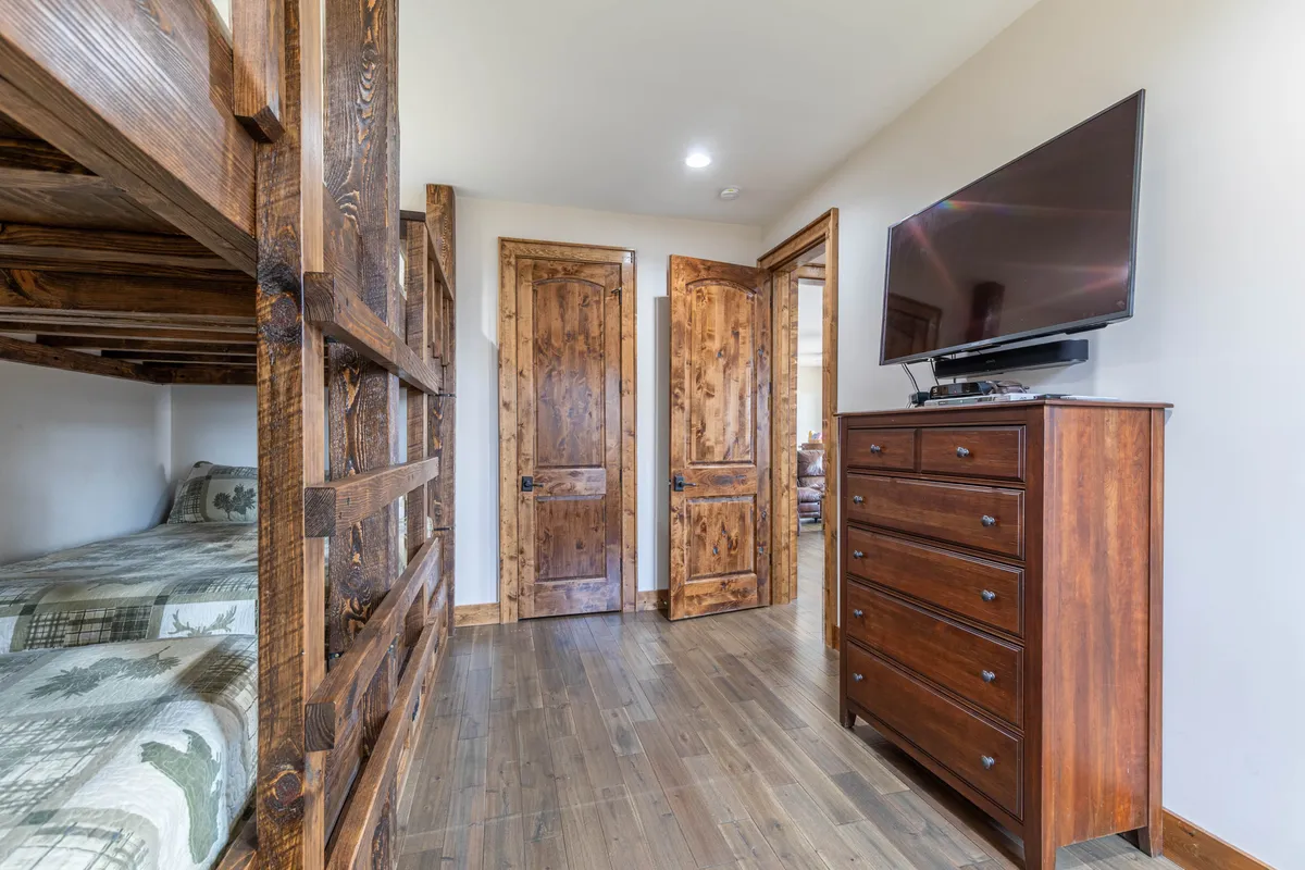 A cozy bunk room outfitted with built-in bunk beds, a chest of drawers, and a wall-mounted TV. The room is designed for relaxation and movie nights, perfect for kids to unwind and enjoy their own entertainment.