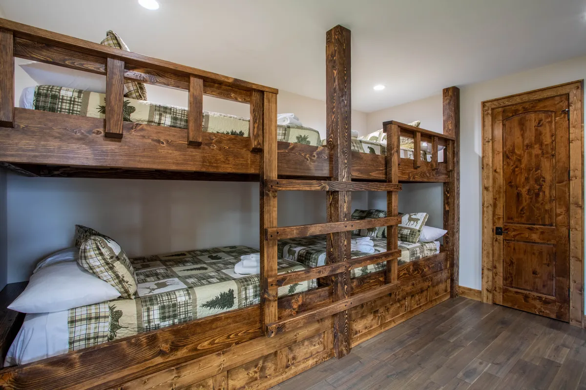 A playful and inviting bunk room with sturdy wooden bunk beds, cozy plaid bedding, and an overall warm, communal feel. The setup is ideal for groups of kids or cousins to share stories, laughter, and lasting memories.