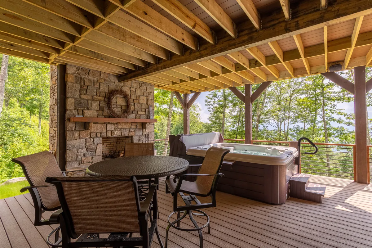 This image showcases a spacious outdoor deck featuring a stone fireplace, an inviting eight-person hot tub, and a large dining table set for al fresco meals. Surrounded by lush trees, the area feels private yet open to mountain air, perfectly framing the outdoor lifestyle described in the section.