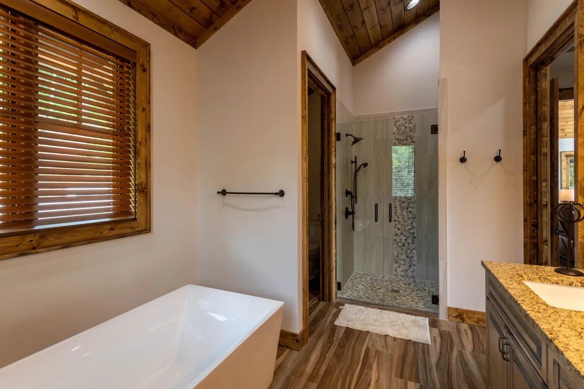 A spa-inspired bathroom with a freestanding soaking tub, walk-in shower, natural wood accents, and granite countertop. The layout is open and accessible, suggesting ease of use and a relaxing environment for self-care routines.