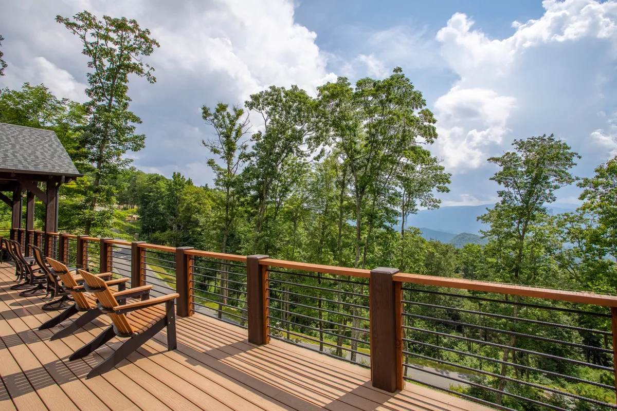 This image captures a wooden deck furnished with adirondack chairs, offering a stunning view of the mountains and lush greenery. The scene is peaceful, highlighting the deck's potential for relaxation, socializing, and soaking in the year-round vistas.