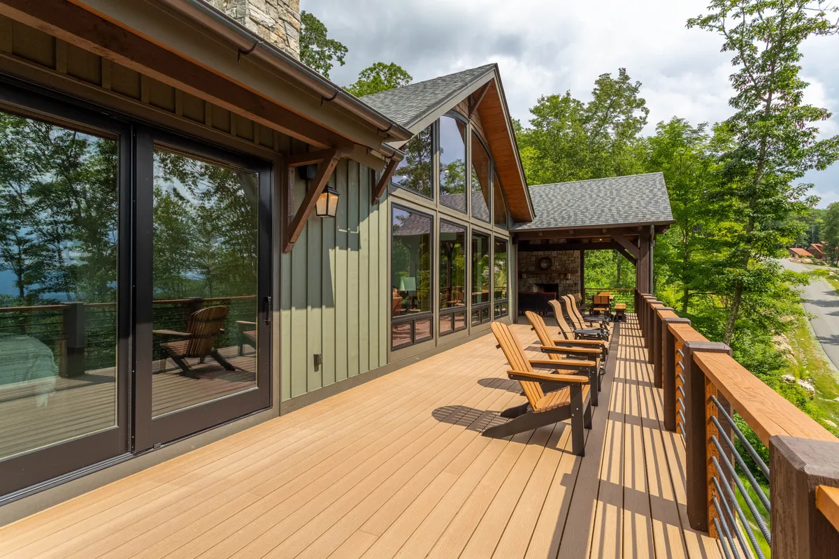 A tranquil wooden deck with comfortable outdoor seating, large glass windows, and sweeping mountain views. The scene suggests an inviting space to relax and enjoy the environment while pets lounge nearby.