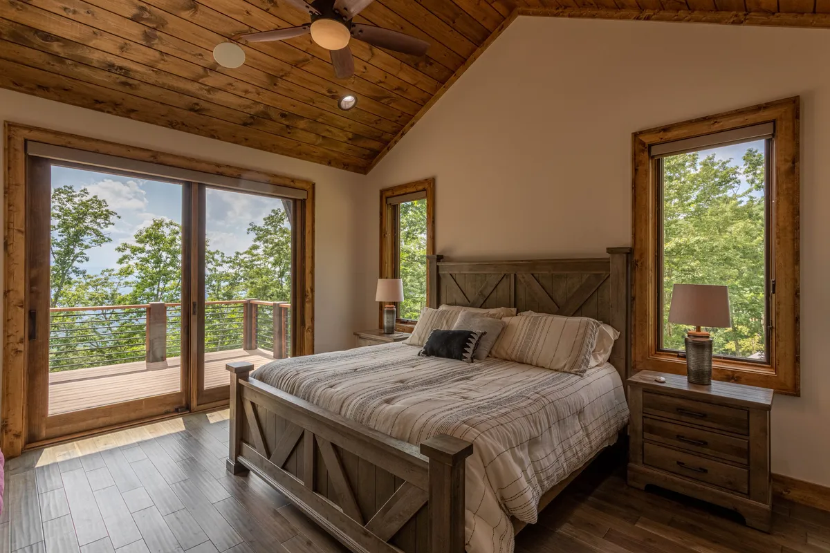 A queen suite with a tranquil mood, featuring a comfortable bed, large windows letting in natural light, and wooden furniture. The view outside provides a serene backdrop for reading or relaxation, ensuring guests find a restful haven.