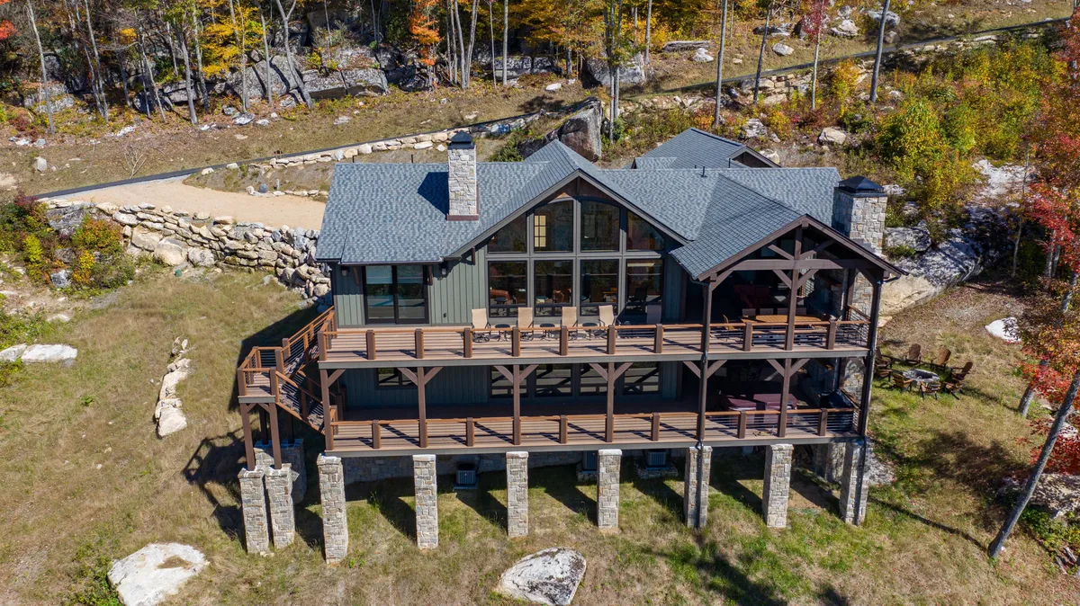 The wooden deck and large windows of Clouds Rest look out over serene trees, with stone pillars adding elegance. The deck offers plenty of space for outdoor relaxation, gatherings, and moving freely between inside and outside.